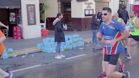 Exhausted-marathon-runners-passing-frame-in-slow-motion-from-right-to-left,-pouring-the-water-on-themselves