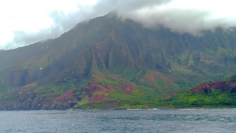 HD-120fps-Hawaii-Kauai-Bootfahren-Auf-Dem-Ozean,-Statisch-Schwebender-Berg-Von-Rechts-Nach-Links-In-Wolken,-Zentriert-Mit-Grünem-Tal-Und-Zeitweiligem-Bootsgischt-überall