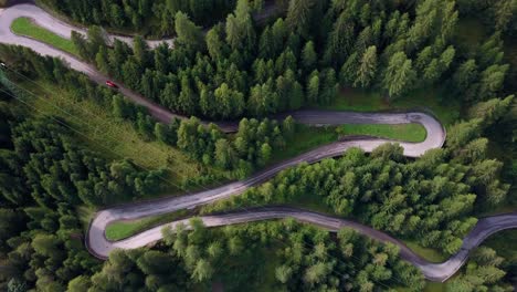 Winding-road-with-red-car-going-up-the-mountain-in-the-Dolomite-area-of-northern-Italy,-Aerial-drone-top-view-rotating-shot