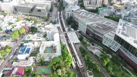 Hong-Kong-MTR-train-arriving-to-station-next-to-a-large-local-shopping-mall,-Aerial-view