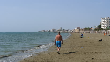 Back-view-of-elderly-man-walking-on-Larnaca-Beach,-Cyprus