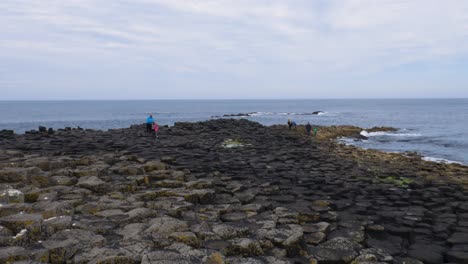 Turistas-Caminando-En-Las-Columnas-Hexagonales-De-Basalto-Con-La-Costa-Norte-Y-El-Cielo-Azul-En-La-Calzada-Del-Gigante-A-Primera-Hora-De-La-Mañana-En-Irlanda-Del-Norte