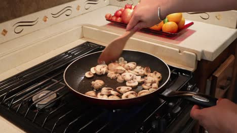 Close-up-of-woman-sauteing-sliced-button-mushrooms-in-a-skillet-in-a-tiny-home-kitchen