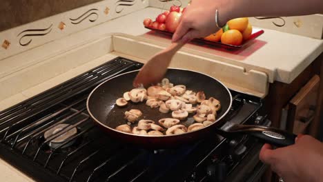 Primer-Plano-De-Una-Mujer-Salteando-Champiñones-En-Rodajas-En-Una-Sartén-En-Una-Pequeña-Cocina-Casera