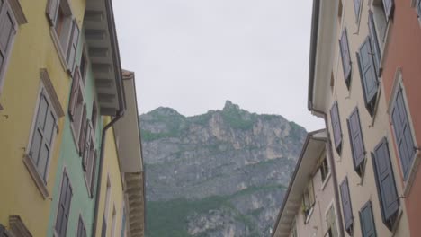 Wunderschöne-Aufnahme-Der-Italienischen-Alpen-Und-Zweier-Farbenfroher-Gebäude-Im-Zentrum-Von-Riva-Del-Garda,-Einer-Kleinen-Stadt-In-Der-Region-Trient-Im-Norden-Italiens
