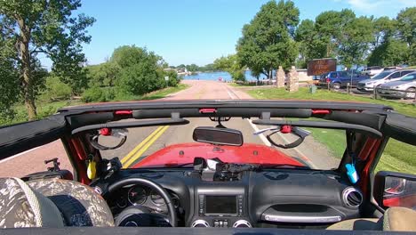 Pov-Conduciendo-Hacia-Y-A-Lo-Largo-De-Un-Lago-En-La-Zona-Rural-De-Dakota-Del-Sur-Con-La-Capota-De-Un-Vehículo-Rojo
