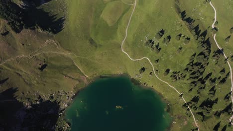 Tilt-up-aerial-shot-over-Seebergsee-in-Switzerland-with-a-small,-tiny-circle-shaped-lake-beneath-with-small-dirt-tracks-and-paths-up-the-mountainside