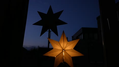 Low-angle-close-up-of-lighting-star-decoration-at-window-with-blue-sky-during-evening-in-background