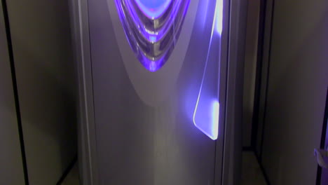 Tilt-up-shot-from-base-to-top-of-a-silver-upright-tanning-machine-with-purple-lights