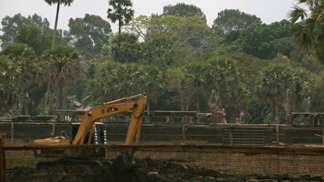 Wide-Shot-of-Digger-in-Front-of-Temple-Pathway-With-Tourists-Walking-Across-the-Screen-in-the-Background-and-Beautiful-Jungle-Behind