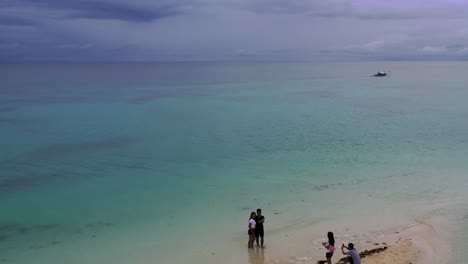 Family-taking-pictures-at-Kota-beach-in-Bantayan-Island-on-a-calm-afternoon,-Aerial-flyover-shot