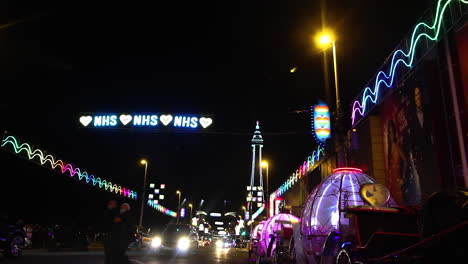 Herz-Nhs-Blinkt-Nachts-Vor-Dem-Mehrfarbigen-Hohen-Blackpool-Tower-An-Einer-Belebten-Straße,-Während-Die-Jährliche-Beleuchtung-Eingeschaltet-Wird