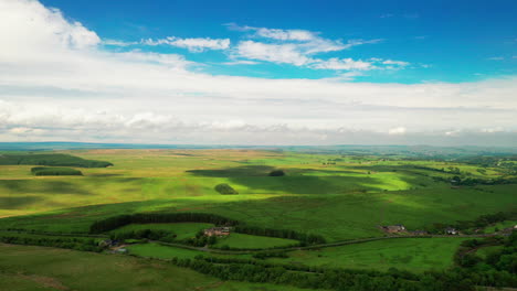 Aerial-landscape-shot-showing-lush-green-farmland,-on-a-bright-blue-sky-day