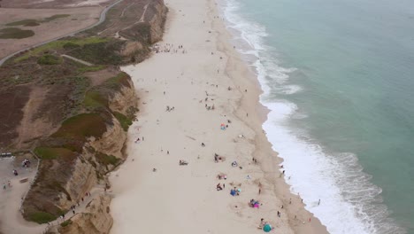 AERIAL:-drone,-half-moon-bay-beach-cliffs-and-people-enjoying-the-beach,-flying-forward-view