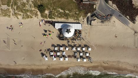 AERIAL:-Top-View-Ascending-Shot-of-Huge-White-Tent-with-Star-on-Rooftop-on-Sandy-Beach