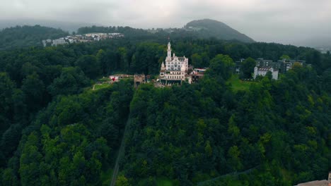 Aerial-view-away-from-the-Chateau-Gutsch-castle,-restaurant-and-hotel,-on-a-hill-in-Luzern-city,-dark,-gloomy,-summer-day,-in-Lucerne,-Switzerland---reverse,-drone-shot