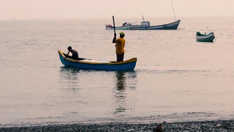 Asian-Fisherman-father-teaching-his-son-to-rowing-a-small-boat-near-a-beach-shore-in-shallow-water,-traditional-small-fishing-boat-rowing-by-a-father-teaching-lesson-to-his-young-son-in-small-boat
