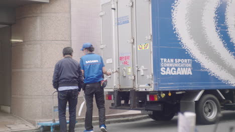 El-Repartidor-Cerró-La-Puerta-Del-Camión-De-Entrega-Urgente-Sagawa-Mientras-Hablaba-Con-Un-Cliente-Frente-A-Un-Edificio-En-Tokio,-Japón