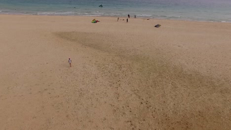 Aerial-view-of-a-beach-with-some-kite-surfers-next-to-the-water-playing-with-the-kites