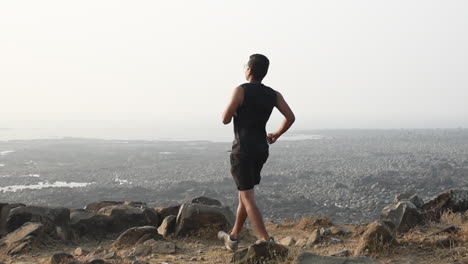 An-South-Asian-young-boy-jogging-and-stopped-near-a-cliff-near-a-beach-enjoying-beach-view-video-background-in-pro-res