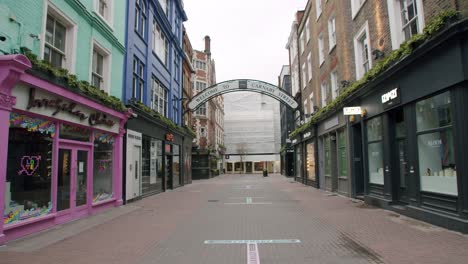 Lockdown-in-London,-deserted-Carnaby-Street-with-closed-shops,-Coronavirus-2-meter-social-distancing-floor-signs-and-welcome-entrance-sign,-during-2020-pandemic