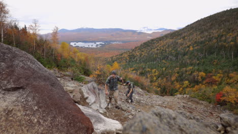 Two-Men-Hiking-up-a-Steep,-Rocky-Mountainside-with-Beautiful-Autum-Colors-in-the-Background,-Adirondack-Mountains-New-York