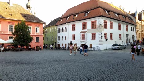 Tourists-walk-across-cobbled-plaza,-Historic-Centre-of-Sighisoara-Romania