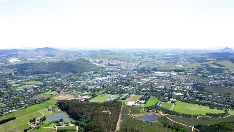 Aerial-drone-Stellenbosch-green-landscape-and-fields-with-forests-and-residential-town-and-neighbourhood-with-houses-and-buildings