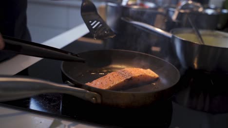 Close-up-shot-of-chef-cooking-fresh-salmon-fish-steak-in-hot-pan-in-kitchen-of-restaurant