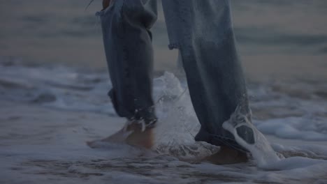 Girl-walking-barefoot-in-long-jeans-along-the-shore-of-the-beach-during-sunset