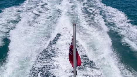 Die-Flagge-Der-Australischen-Red-Ensign-Weht-Gegen-Die-Wellen-Eines-Bootes,-Das-In-Offenen-Gewässern-Segelt