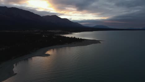 Kluane-Lake-and-mountains-silhouetted-during-winter-sunset,-drone-shot