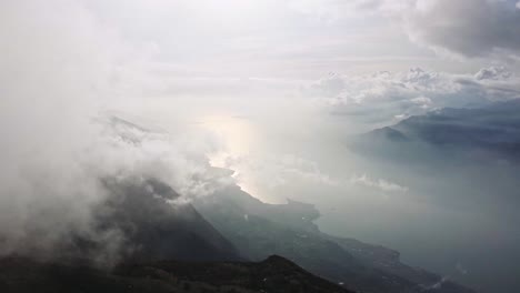 blue-Garda-lake-emerges-from-white-clouds-and-fog,-Italian-landscape,-aerial