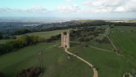 Wide-aerial-pull-out-rising-reveal-shot-of-Broadway-tower,-an-English-landmark-stood-atop-Beacon-Hill-in-the-Cotswolds,-UK
