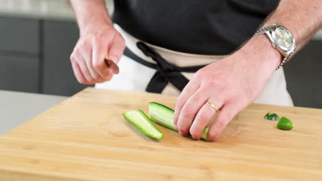 Male-model-slicing-the-cucumber-with-extremely-sharp-knife-on-the-cutting-board-at-the-kitchen
