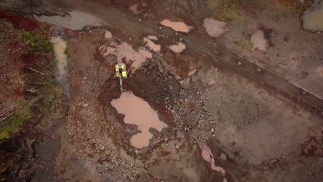 Excavator-working-in-stone-quarry,-top-down-aerial-view