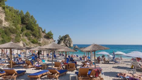 Schwenk-Eines-Malerischen-Griechischen-Strandes,-Parga,-Kleiner-Strand-Mit-Türkisfarbenem-Wasser,-überfüllt-Von-Touristen