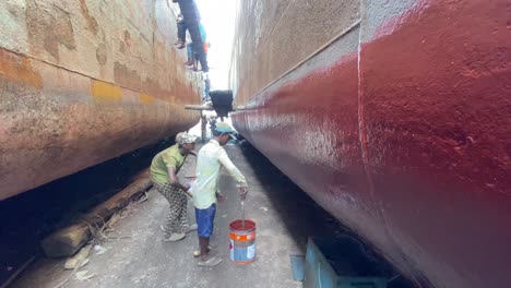 Hand-held-shot-of-ship-workers-painting-the-hull-with-fresh-paint-in-a-shipyard