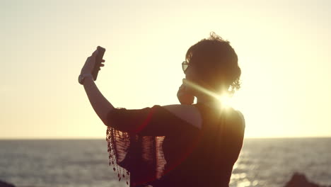Woman-taking-a-selfie-in-front-of-an-ocean-sunset-in-slow-motion
