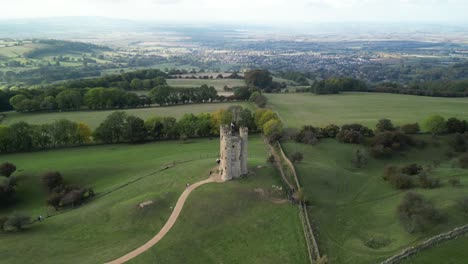 Dramatic-wide-aerial-shot-pushing-into-Broadway-tower,-an-English-landmark-stood-atop-Beacon-Hill-in-the-Cotswolds,-UK