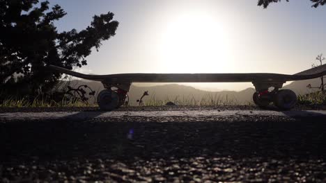 Schwenkaufnahme-Eines-Skateboards-Bei-Sonnenuntergang-In-Den-Bergen-Am-Straßenrand