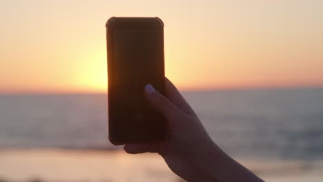 Woman-taking-video-of-an-ocean-sunset-with-mobile-phone,-Rabat-Morocco