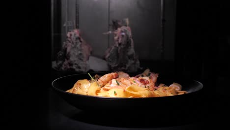 Delicious-shrimp-ragout-with-pasta-rotating-on-black-plate-isolated-on-dark-background