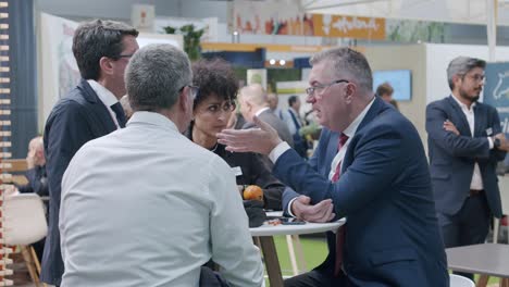 Group-of-co-workers,-sitting,-discussing-around-desk,-trade-show,-Madrid,-Spain