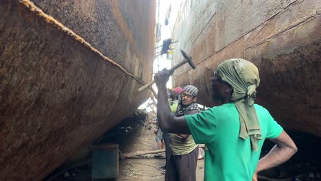 Close-up-shot-of-workers-banging-the-rust-off-of-a-ships-hull-in-a-shipyard