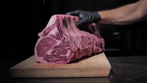 Professional-chef-puts-piece-of-raw-meat-on-wooden-board-and-cuts-for-steak