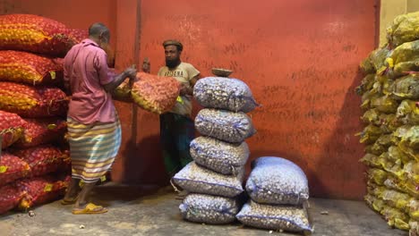 2-workers-lifting-then-carrying-a-sack-of-ginger,-onion,-garlic,-on-his-head-from-inside-a-storage-area-to-outside