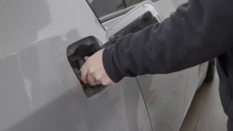 Gas-station-white-caucasian-man-with-wedding-ring-filling-up-silver-car-pressing-and-opening-fuel-tank-cover-and-twisting-removing-gas-cap-and-turning-towards-pump