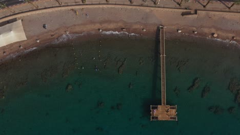Relaxing-protected-coral-reef-marine-park-and-crystal-clear-waters-famous-under-a-long-pier-for-tourism,-scuba-diving-and-viewing-marine-life-in-the-Red-Sea-Eilat-Israel,-panning-left-drone-shot
