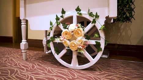 artistic-designed-wheel-with-yellow-roses-flowers-and-green-wheels-minimalistic-clean-white-attached-to-table-full-f-desserts-feet-of-woman-walking-closer-to-it-hired-for-the-wedding-event